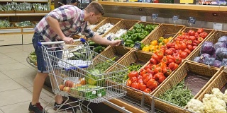 在超市里推着购物车的年轻人。有人在杂货店挑选新鲜蔬菜，然后把它们放进购物车。男孩在商店买辣椒