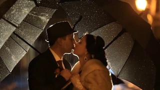 美丽的黑色风格的情侣在雨中亲吻夜晚的城市街道，在雨伞下躲避雨滴视频素材模板下载