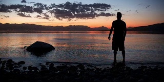 一个人的剪影扔石头的湖和美丽的日落在山上