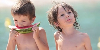 两个小孩，男孩兄弟，夏天的时候在海滩上吃西瓜