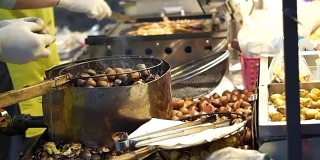 小贩在街头小吃摊上烤鱿鱼和剥烤栗子。亚洲秋食