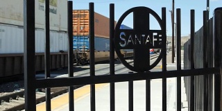 A freight train passes a Santa Fe iron gate in a rail yard  on a railroad in Arizona