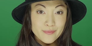 美丽的年轻亚洲女人戴着一顶帽子和微笑，在一个绿色屏幕的工作室背景