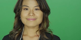 年轻的亚洲女人微笑愉快，在一个绿色屏幕的工作室背景