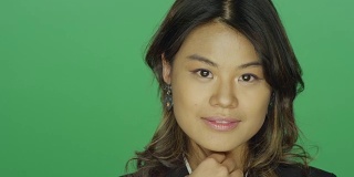 年轻的亚洲女人微笑着把她的头发放在她的头发后面，在一个绿色的屏幕工作室背景