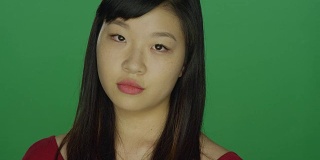 年轻的亚洲女人看起来严肃，在一个绿色屏幕的工作室背景