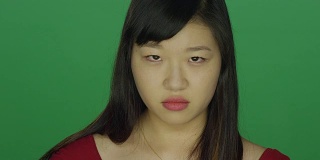 一个年轻的亚洲女人看起来生气和恼怒，在一个绿色屏幕的工作室背景