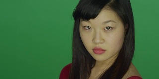 一名年轻的亚洲女子转过身来，盯着录音室背景的绿色屏幕上的摄像机
