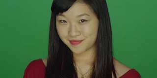 年轻的亚洲女人微笑和调情，在一个绿色屏幕的工作室背景