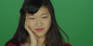 一个年轻的亚洲女人看起来非常沮丧和恼怒，在一个绿色屏幕的工作室背景