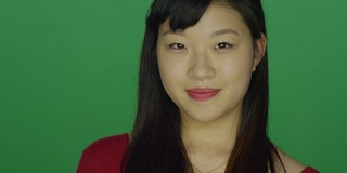 年轻的亚洲女人微笑愉快，在一个绿色屏幕的工作室背景
