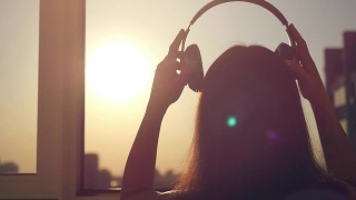 年轻女子戴上耳机，听音乐，跳舞，看城市日落的慢动作视频素材模板下载