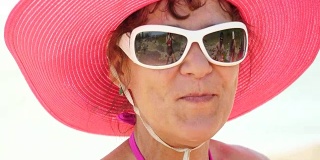 戴着帽子和太阳镜的时髦女士在海上微笑，吃西瓜