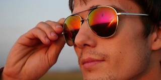 帅气的年轻时尚男子戴着太阳镜，看起来日落在野外