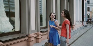 年轻女孩的朋友们站在商店橱窗旁边，拿着婚纱聊天。缓慢的莫