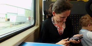 一名女子在行驶的火车上用手机阅读电子邮件。一个女人带着她的男婴旅行。一名女子用手机看新闻的偷拍照片。