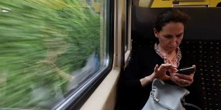 一位忧心忡忡的女士在坐火车上下班时查看手机。火车上的女乘客一边用手机工作一边看手机