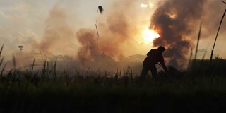 在巴厘岛乌布，农民和妇女的剪影在稻茬燃烧的烟雾中经过