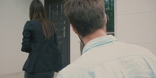 一对年轻的夫妇跟着一个健谈的黑发女人来到一幢白色大房子的前门。慢动作，斯坦尼康镜头