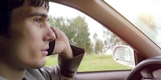 年轻英俊的黑发男子开着车在田野里，用手机慢动作说话。高清。1920 x1080
