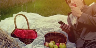 年轻英俊的商人在公园野餐。一名男子用装满苹果的手机打电话。FullHD