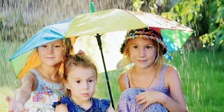 三个欢快无忧无虑的女孩撑着彩虹色的伞。有一场温暖的雨。快乐的童年