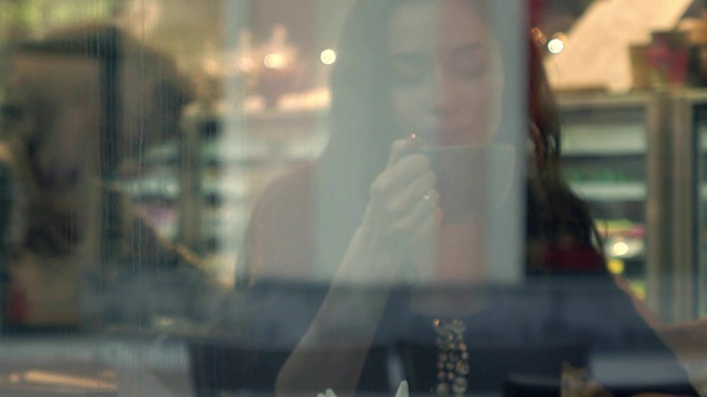 美丽的黑发女孩在小咖啡馆喝热巧克力。窗外的景色。FullHD视频