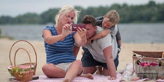 美丽的家人在海滩上用手机自拍
