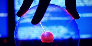 等离子球-充满稀薄惰性气体的透明球体。手的慢动作触摸等离子球对蓝色背景的破电脑