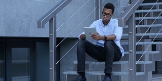 年轻黑人坐在楼梯上浏览平板电脑
