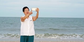 亚洲资深女性放松和谈论自拍在海洋海滩