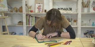 女人正用彩色铅笔坐在书桌前画图画或卡片