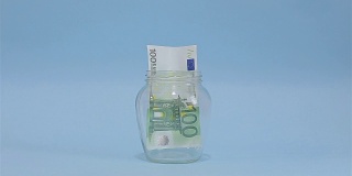 一名男子将欧元放入玻璃罐中储存。浅蓝色背景上的槽式玻璃罐。