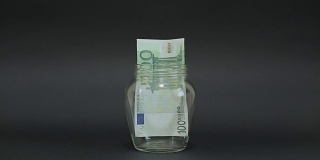 一名男子将欧元放入玻璃罐中储存。黑色背景上的槽式玻璃罐。