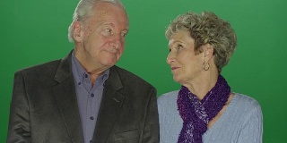 在一个绿色的画室背景上，一对年长的夫妇互相看了看，笑了