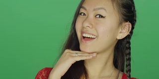 年轻的亚洲女人微笑和顽皮，在一个绿色屏幕的工作室背景