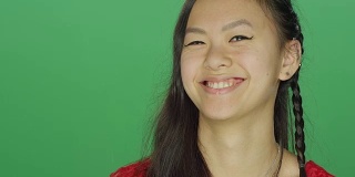 年轻的亚洲女人微笑和顽皮，在一个绿色屏幕的工作室背景