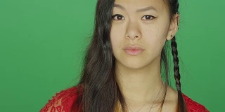 一个年轻的亚洲女人盯着，看起来很严肃，在一个绿色屏幕的工作室背景