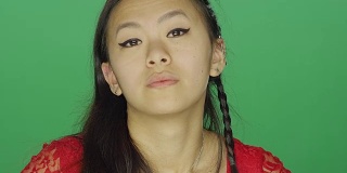 一个年轻的亚洲女人盯着，看起来很严肃，在一个绿色屏幕的工作室背景