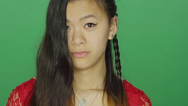 年轻的亚洲妇女环顾四周，做着傻傻的脸，在一个绿色屏幕的工作室背景