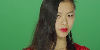 年轻的亚洲女人盯着和看起来性感，在一个绿色屏幕的工作室背景