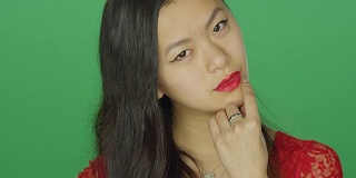 年轻的亚洲女人盯着和调情，在一个绿色屏幕的工作室背景