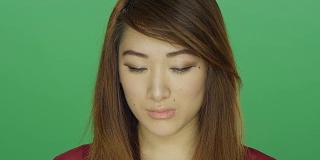 年轻的亚洲女人看起来很悲伤，在一个绿色屏幕的工作室背景