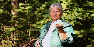 一位上了年纪的妇女在森林里展示珊瑚蘑菇