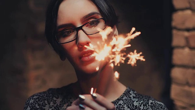 年轻的哥特女人的肖像，黑色短发，戴眼镜。他看着一个燃烧着的火花