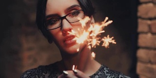 年轻的哥特女人的肖像，黑色短发，戴眼镜。他看着一个燃烧着的火花
