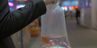 近距离观看女人的手臂拿着塑料包装的金鱼和去购物中心。中国香港