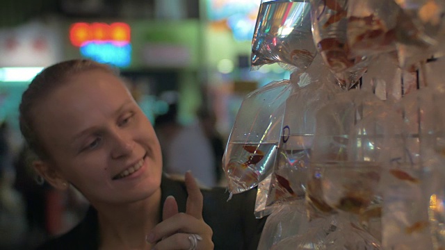 年轻的金发女人拍了一张装在塑料袋里的金色鱼缸鱼的照片。中国香港