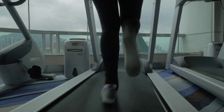 近距离观看妇女在跑步机上在健身中心看窗户与城市景观。中国香港
