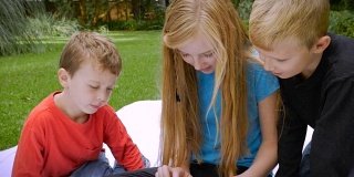 三个年幼的孩子完全沉浸在他们共享的平板电脑上——慢动作